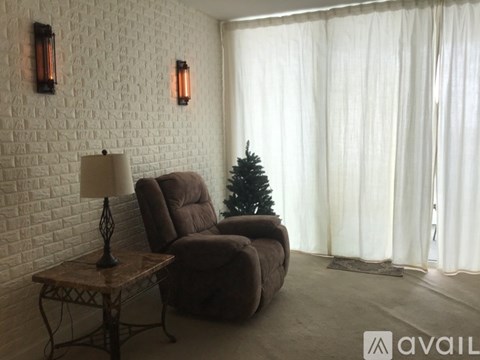 A living room with a brown chair, a table with a lamp, and a small Christmas tree.