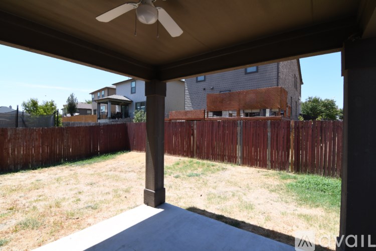 A patio with a ceiling fan and a view of a backyard with a fence.