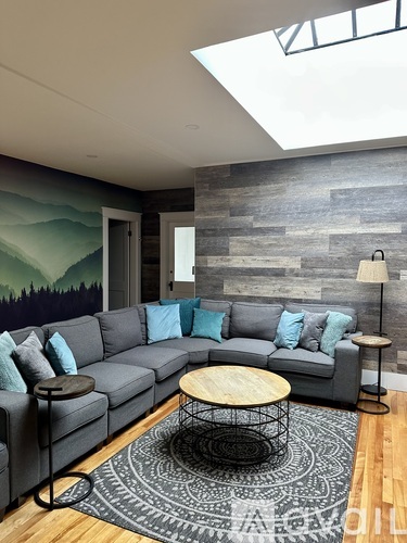 A grey couch with blue pillows sits in front of a grey wall with a mountain mural.