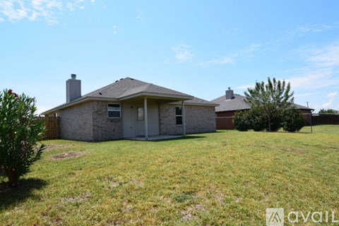 A house with a brown roof and a white door is surrounded by a grassy lawn.