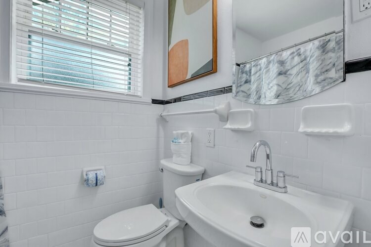 A white bathroom with a toilet, sink, and a window with blinds.