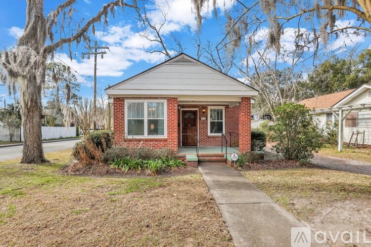 A small red brick house with a porch and a tree in front.