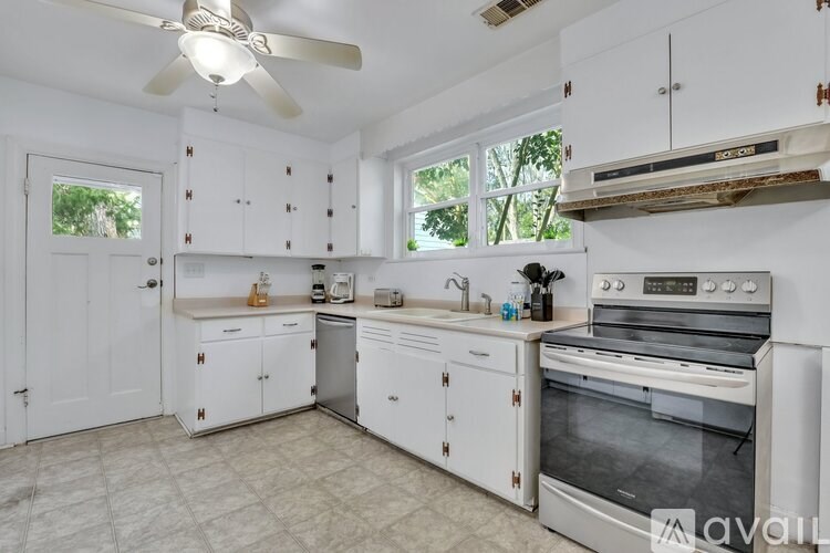 A kitchen with white cabinets and appliances, a ceiling fan, and a window.