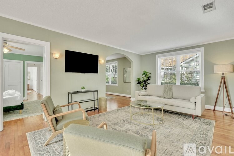 A living room with a white couch, a chair, a coffee table, and a flat-screen TV mounted on the wall.