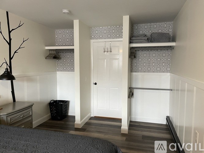 A room with a bed, a dresser, a trash can, a tree decoration, a wall shelf, and a door.