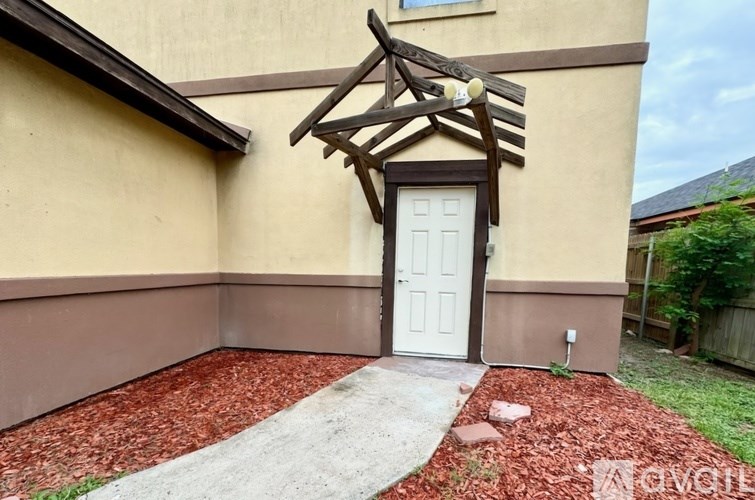 A white door is flanked by a wooden canopy and a red brick pathway.