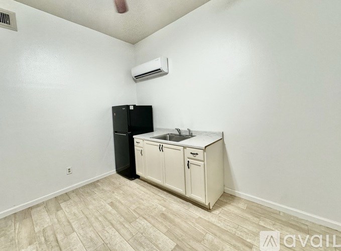 A kitchen area with a black fridge, white cabinets, and a wooden floor.