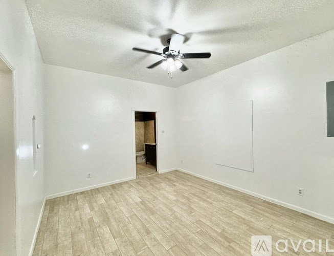 A room with a ceiling fan and light, hardwood floors, and white walls.