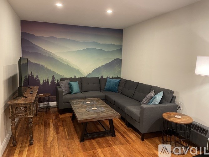 A living room with a grey couch and a mountain mural on the wall.