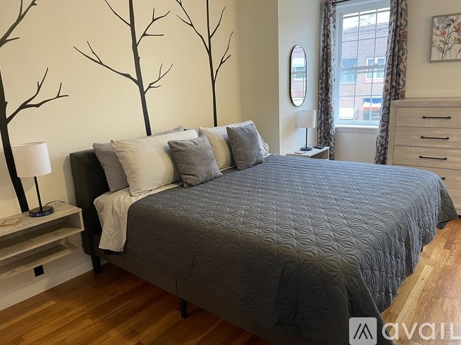 A bedroom with a large bed and a tree mural on the wall.