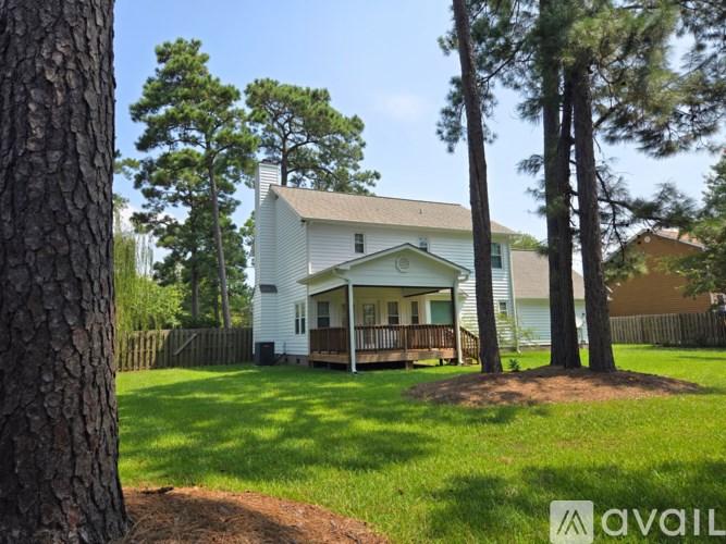 A house with a white exterior and a porch surrounded by trees.