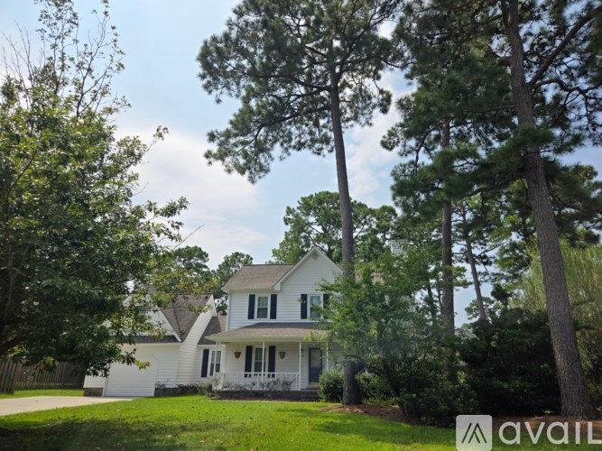A house with a white exterior and a porch is surrounded by trees and has a sign that says "AVAILABLE".