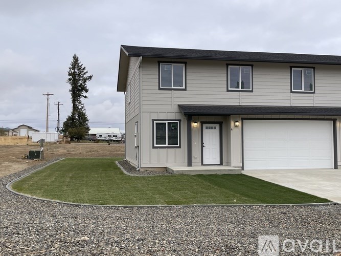 A grey house with a white garage door and a gravel driveway.