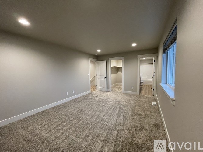 A spacious room with carpeted flooring and a window on the right side.
