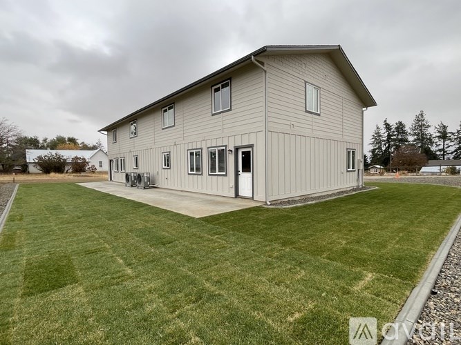 A house with a grey exterior and a white door is surrounded by a grassy lawn.