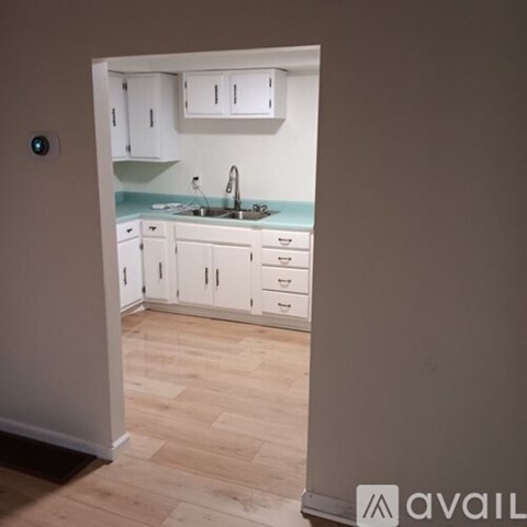 A kitchen with white cabinets and drawers is visible from an open door.