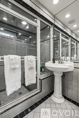 A white pedestal sink with a mirror above it and towels hanging on the glass door.