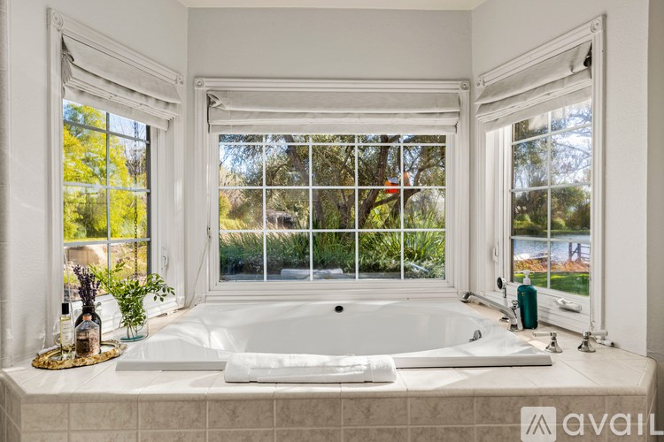 A bathroom with a large tub and a view of trees and a body of water.