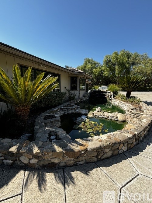 A house with a stone wall and a water feature in the front yard.