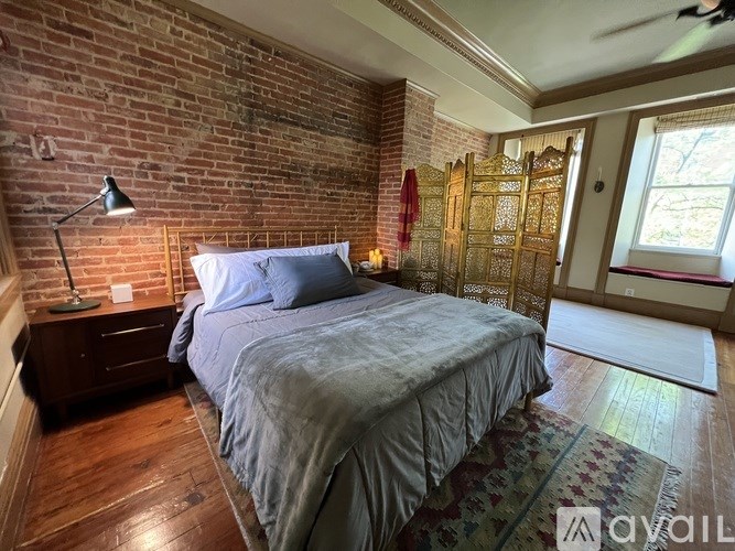 A bedroom with a brick wall and a bed with a grey comforter.