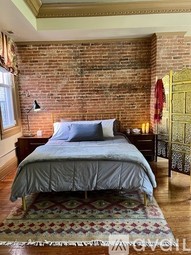 A bedroom with a brick wall and a bed with a blue comforter.