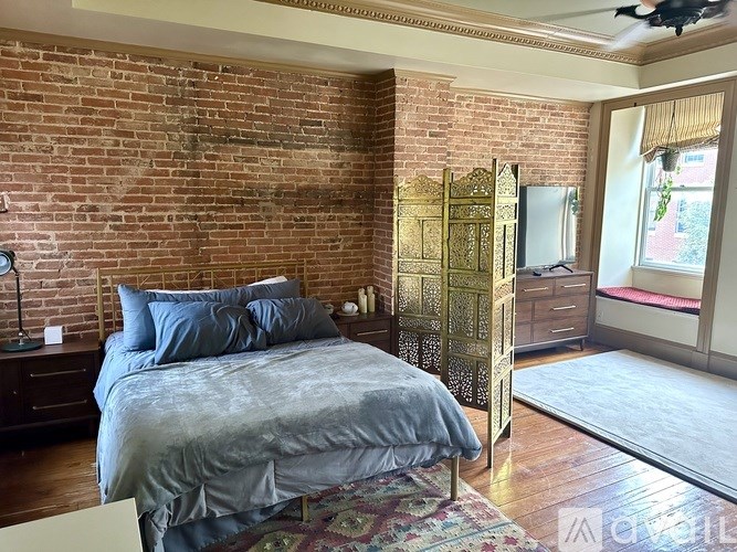 A bedroom with a brick wall and a bed with a grey comforter.