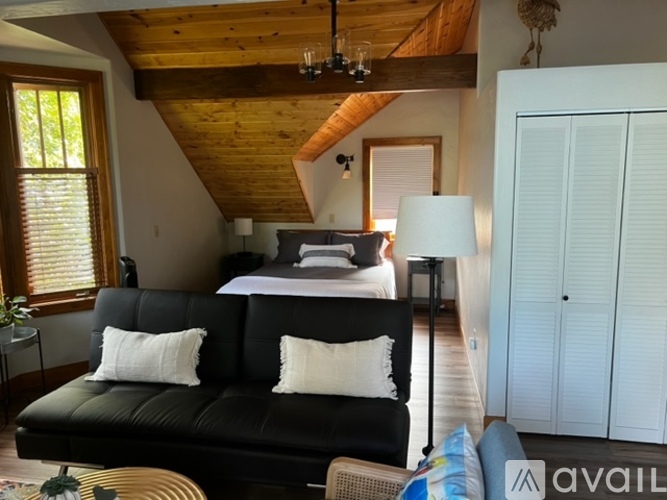 A bedroom with a black leather couch and a wooden ceiling.