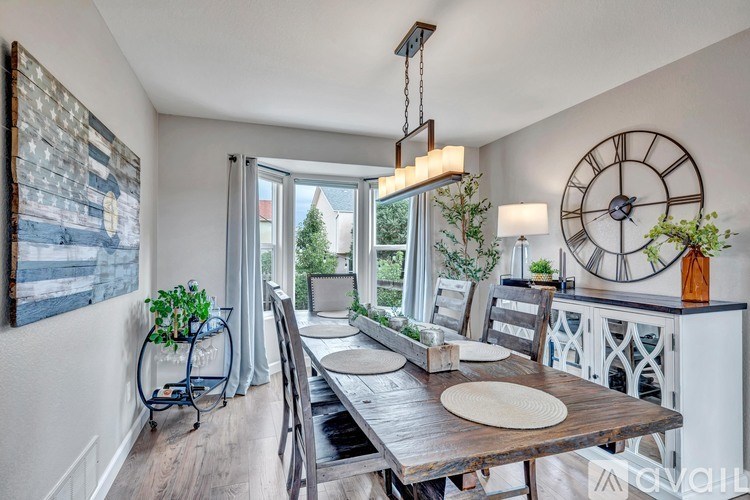 A dining room with a wooden table and chairs, a hanging plant, and a large clock on the wall.