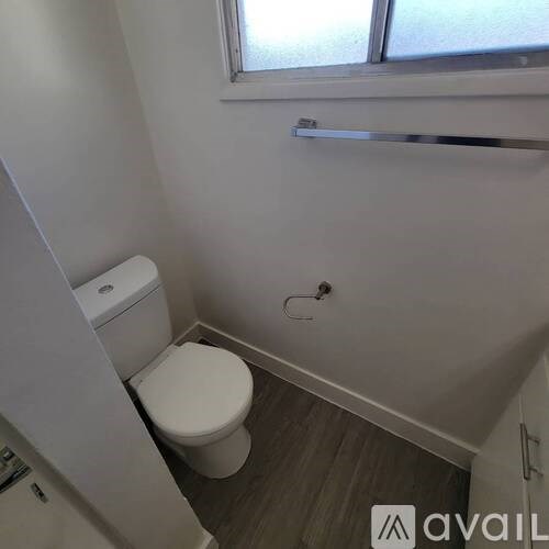 A white toilet in a small bathroom with a window above it.