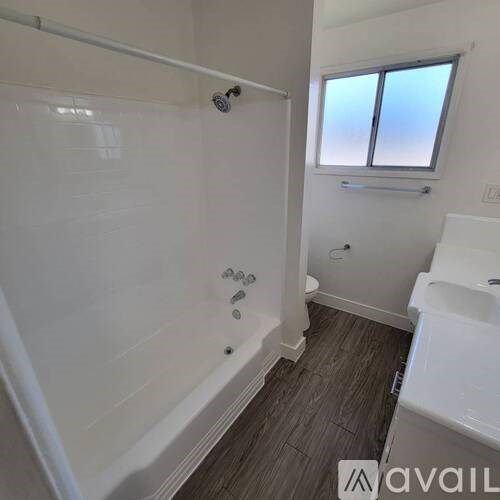 A white bathroom with a tub, sink, and window.