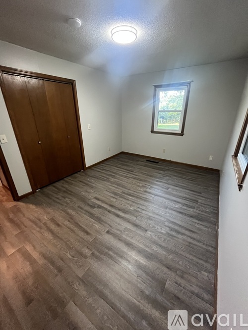 A room with a wooden floor and a window with a view of trees.