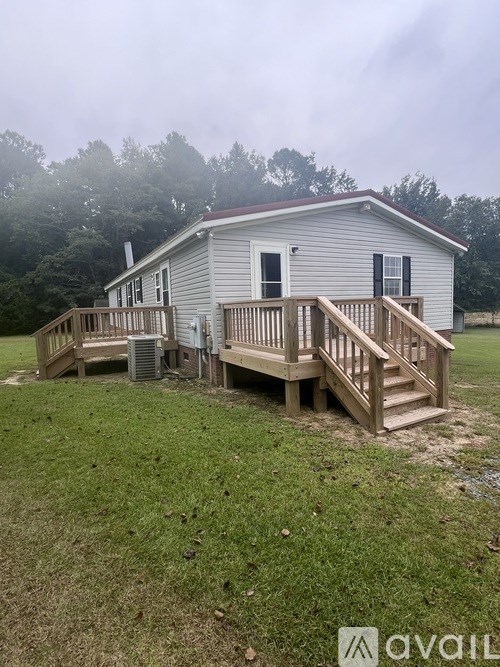 A house with a porch and a deck is surrounded by grass and trees.