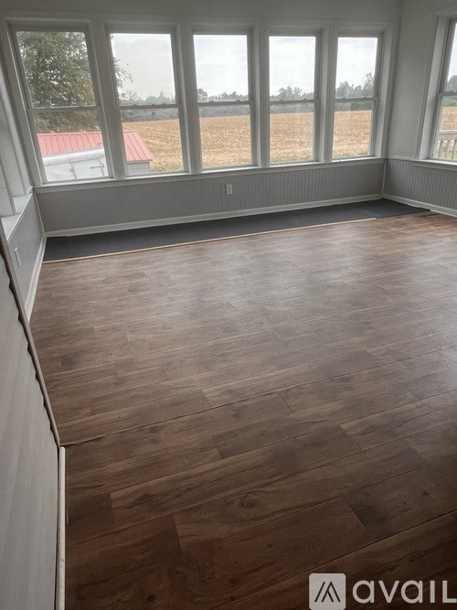 A room with wooden flooring and large windows overlooking a field.
