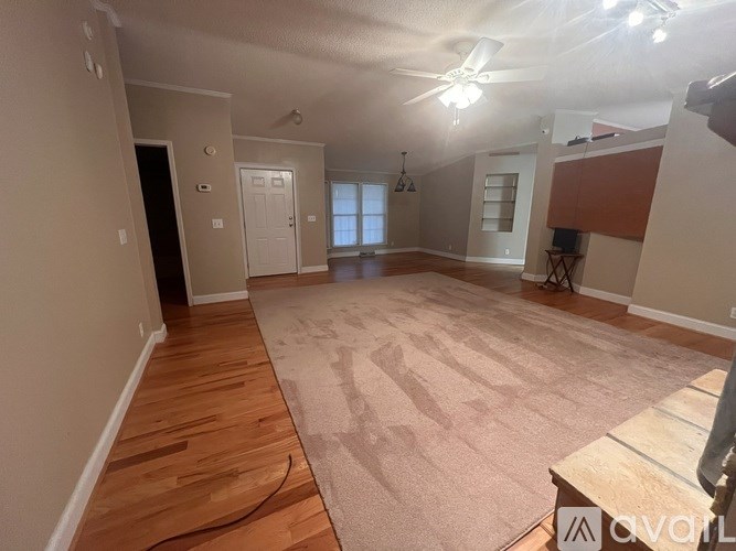 A spacious room with wooden flooring and a rug in the center.