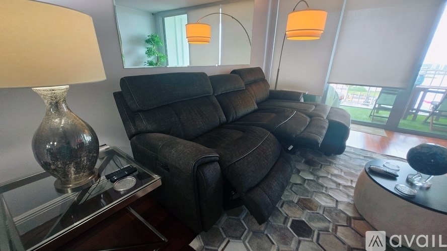 A living room with a black sofa and a glass table with a lamp on it.