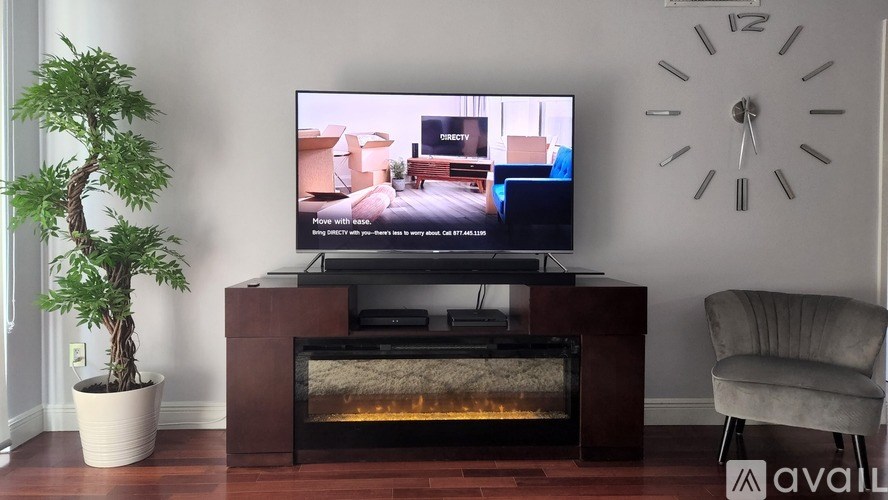 A modern living room with a flat screen TV, a fireplace, a potted plant, and a wall clock.