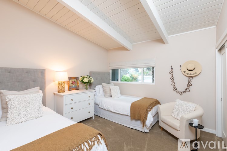 A bedroom with a white bed, a white chair, and a window with a view of trees.