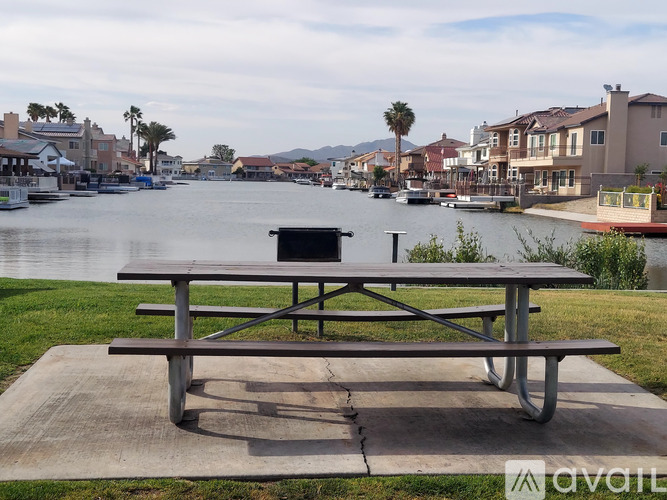 A picnic table is in the foreground of a body of water with houses and palm trees in the background.
