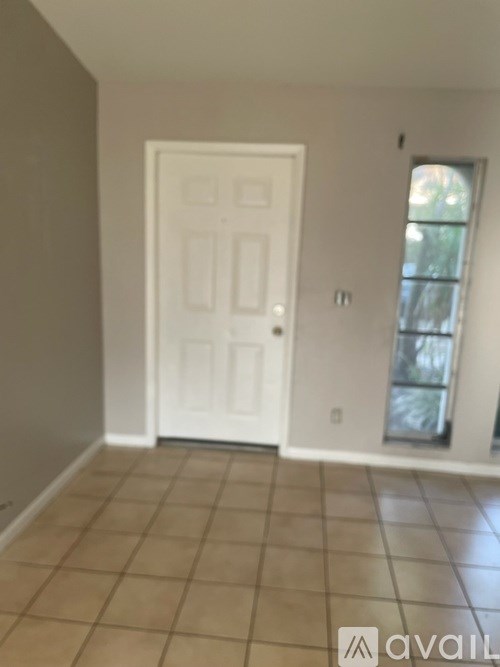 A white door is in a room with tile flooring and a window.