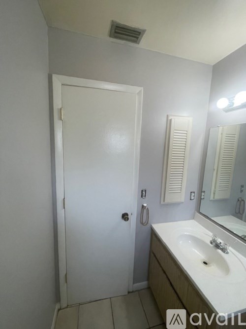 A bathroom with a white door, sink, and mirror.