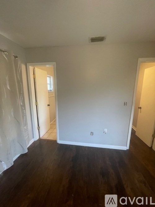 A room with wooden floors and white walls, with a door on the left and a window on the right.
