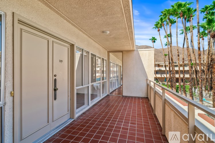 A balcony with a red tile floor and a view of palm trees.