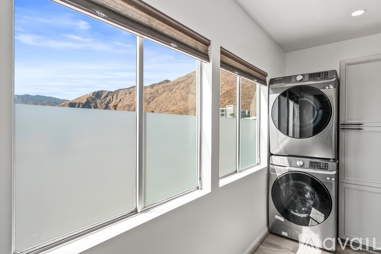 A modern laundry room with a washer and dryer, a window with a view of a mountain, and a glass door.