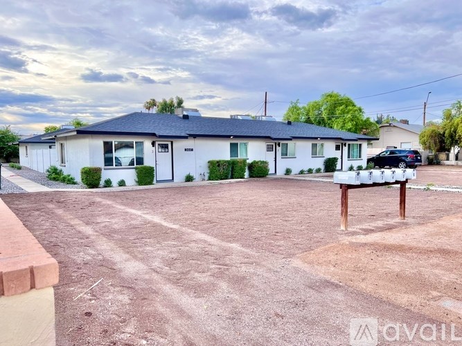 A house with a white exterior and a black roof is surrounded by a dirt lot.