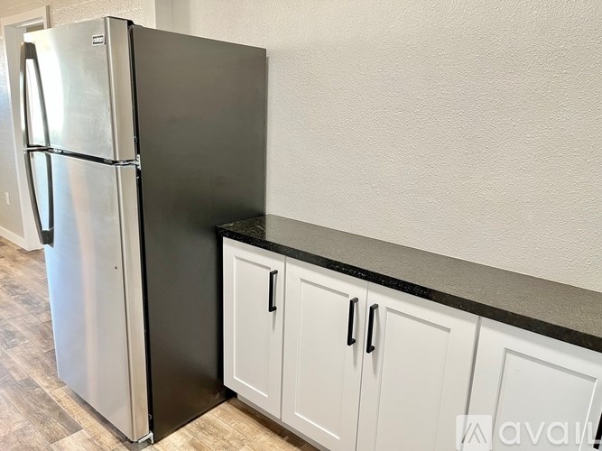 A black fridge in a kitchen with white cabinets.