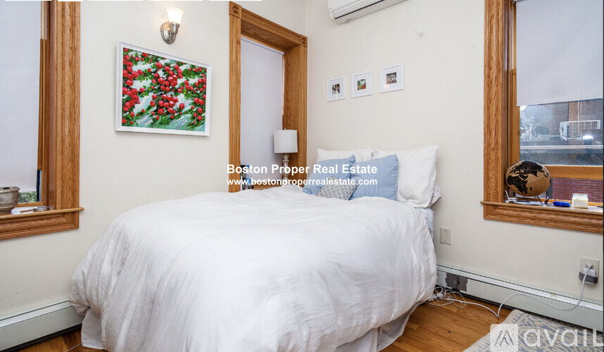 A bedroom with a white bed and a painting of red flowers on the wall.