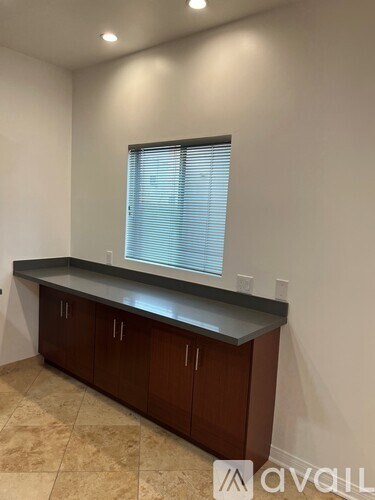 A kitchen area with brown cabinets and a window with blinds.
