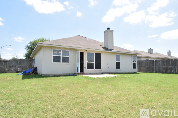 A house with a brown roof and a chimney is surrounded by a fence and has a blue tarp on the lawn.