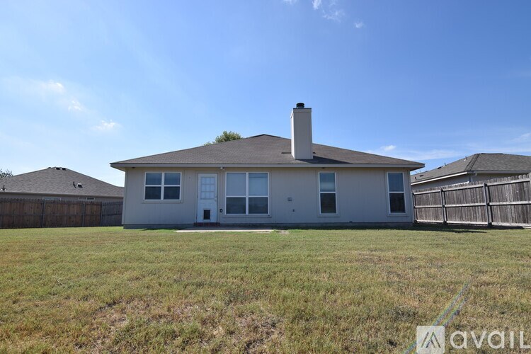 A house with a brown roof and a chimney is surrounded by a fence and grassy field.