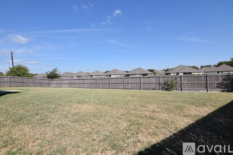A grassy field with a fence and houses in the background.